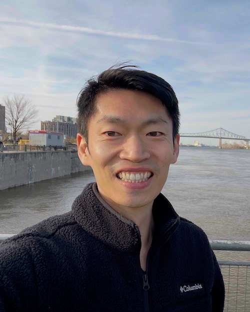 Jack Liu, smiling, standing by the water on a cloudy day