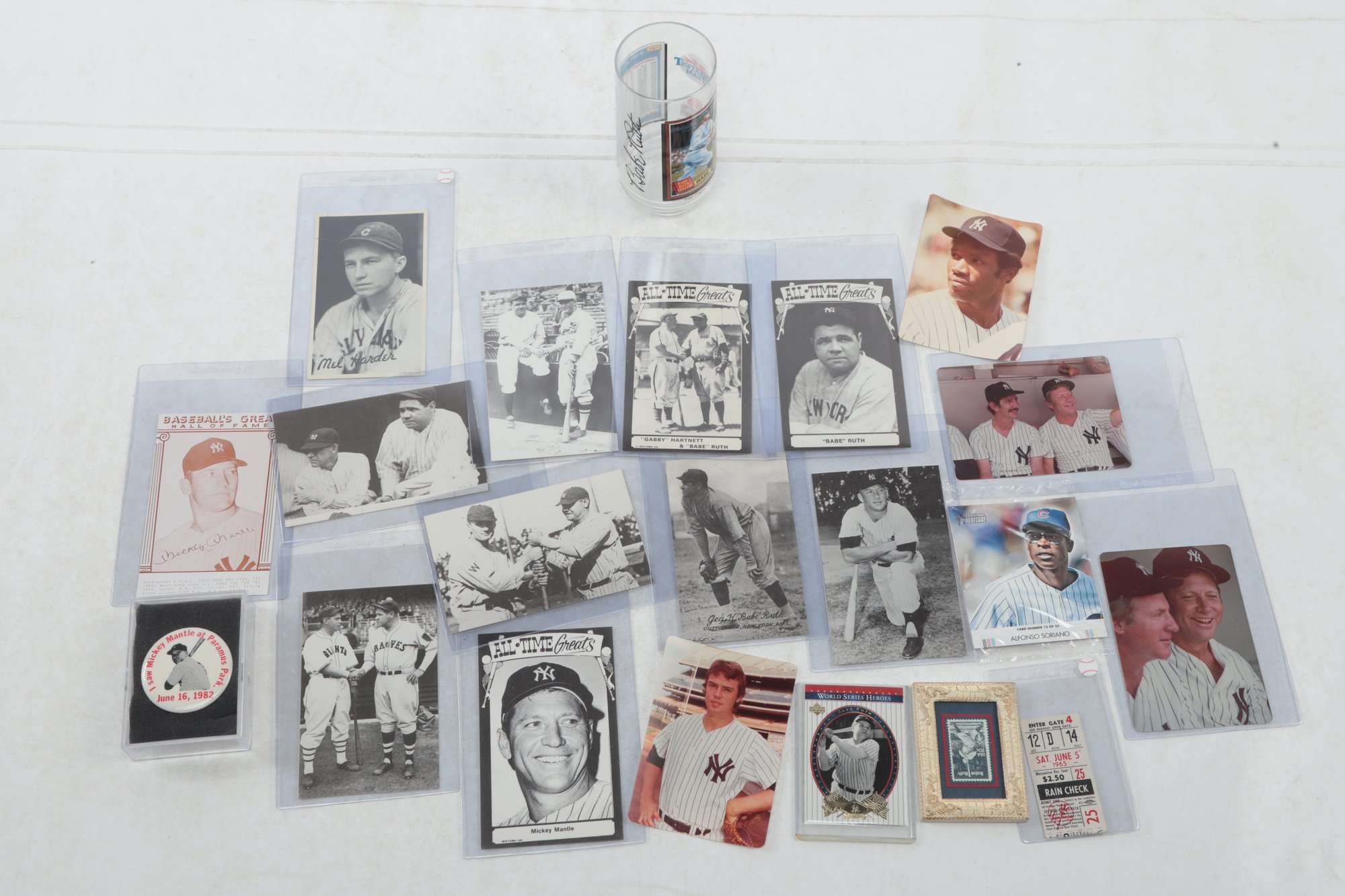 Vintage Babe Ruth and Mickey Mantle cards and photos in sleeves, with an old Yankees rain check and a Mantle pin